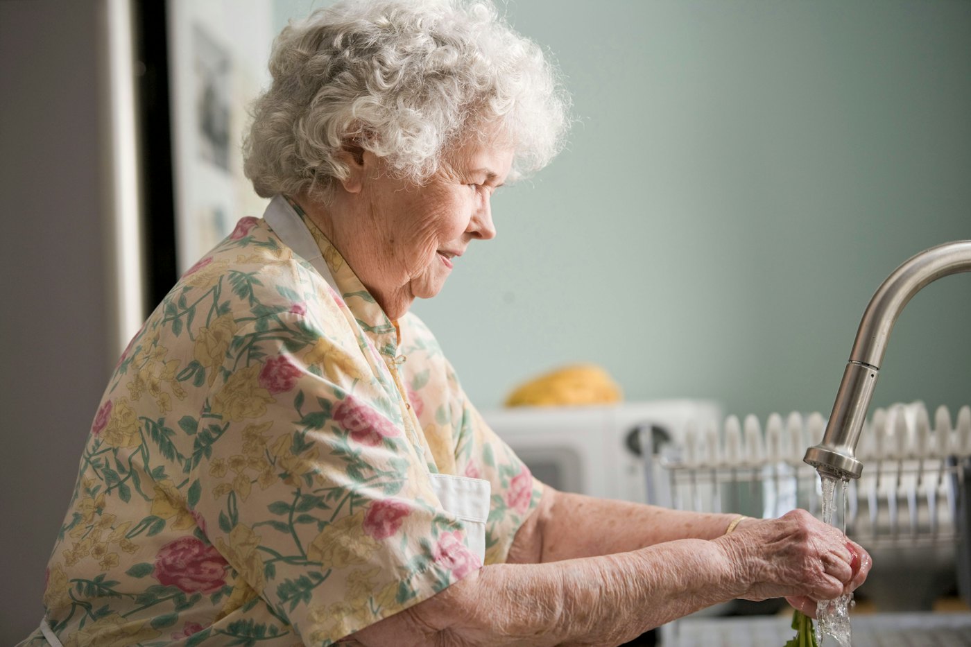 An older woman washing up at her kitchen sink