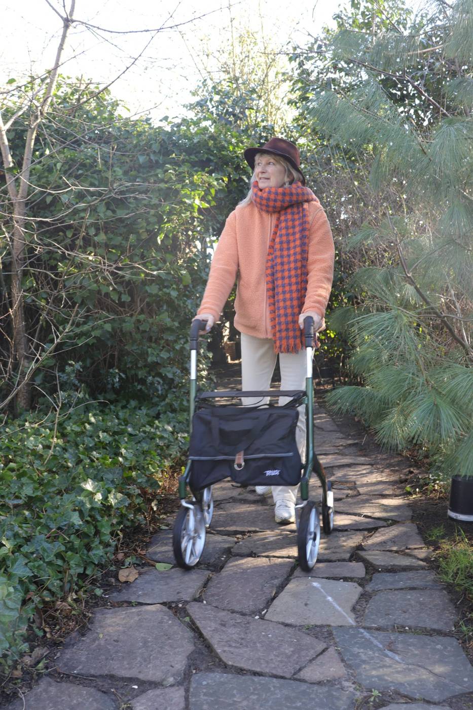 An older woman walking with her walker along a garden path